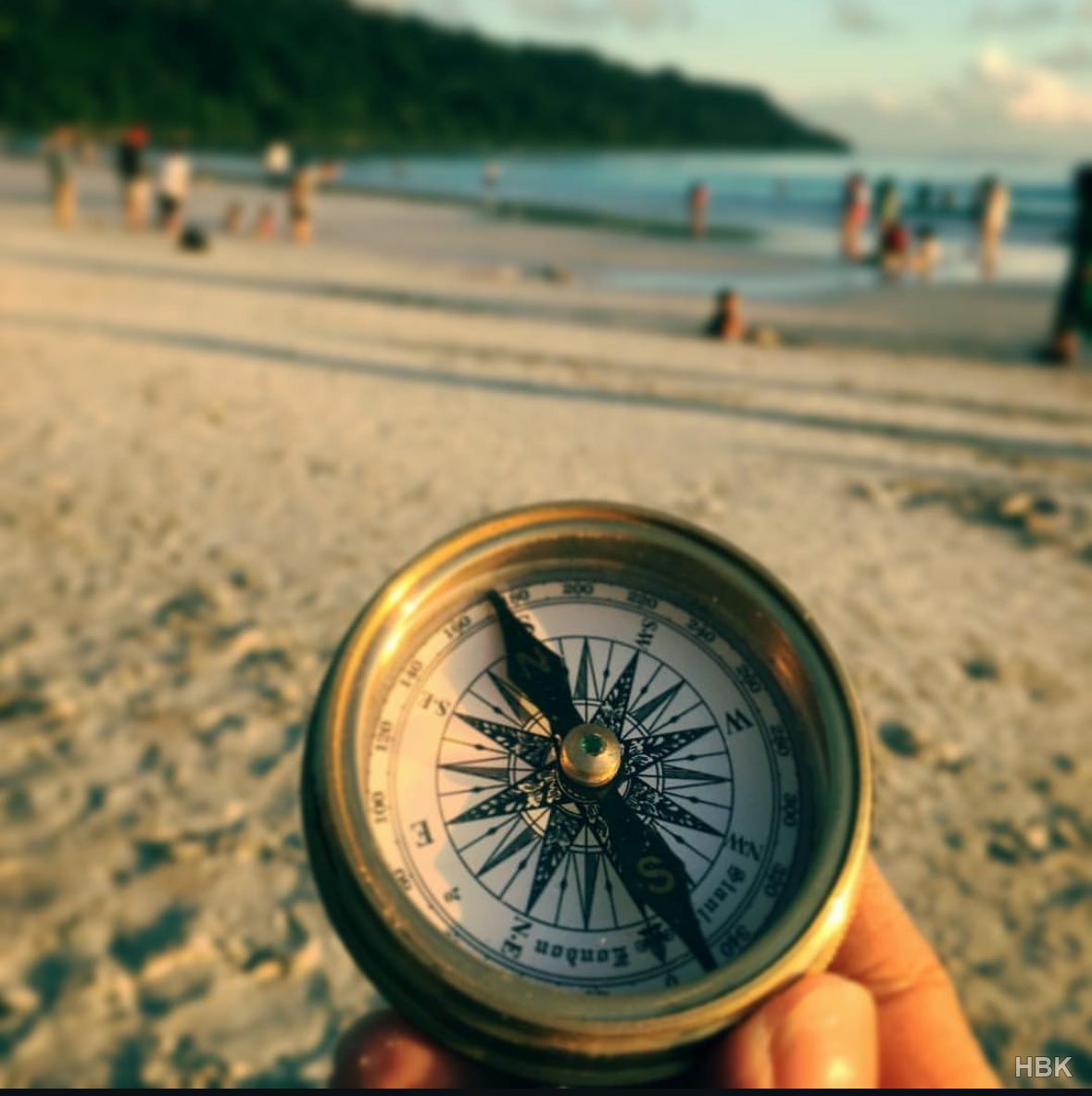 Hand holding a brass compass with a beach in the background