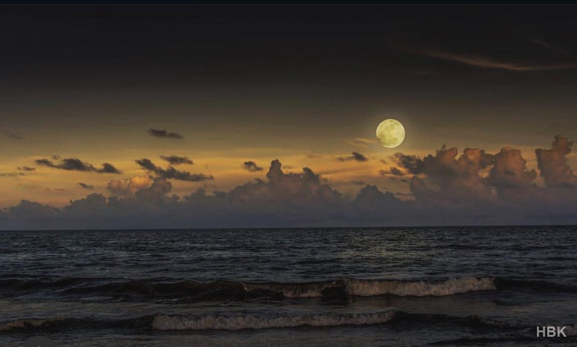 Moon above clouds and waves on a dark coastline