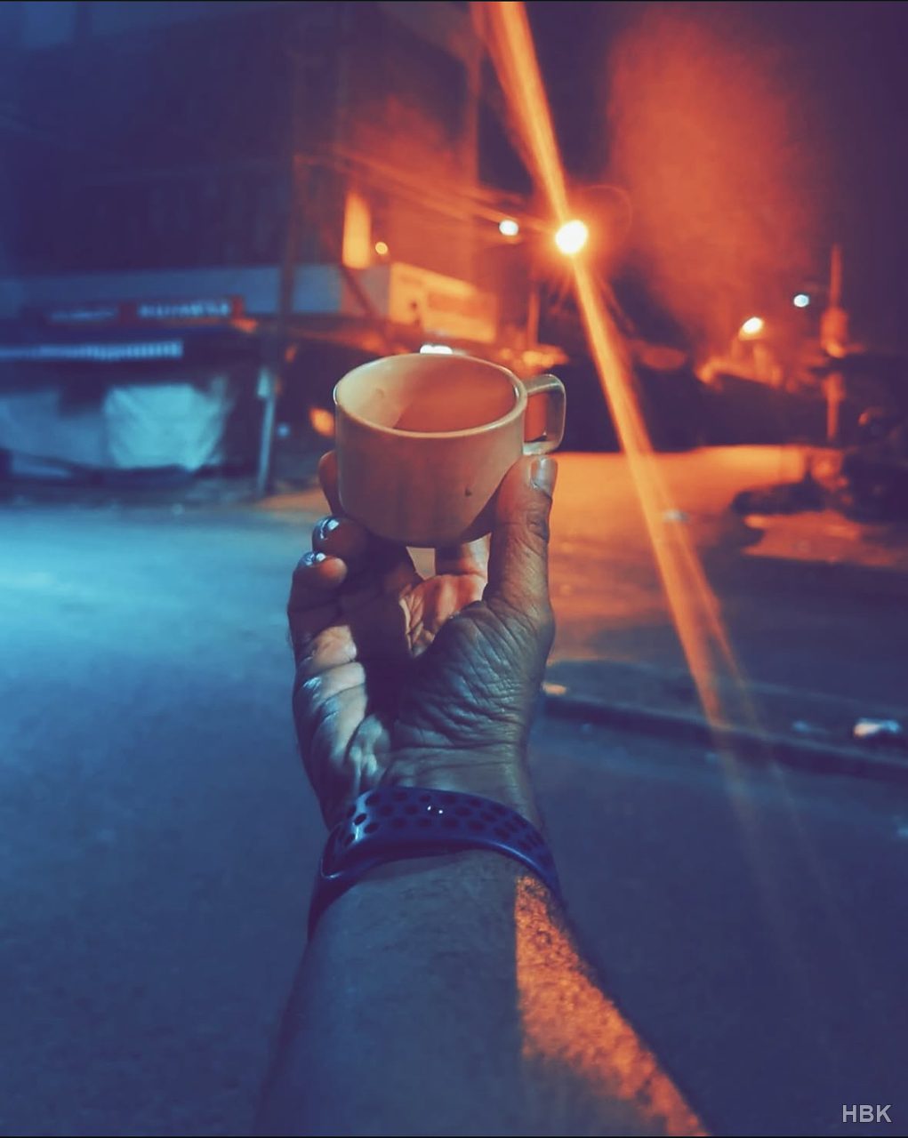 Hand holding a cup beneath warm streetlights at night